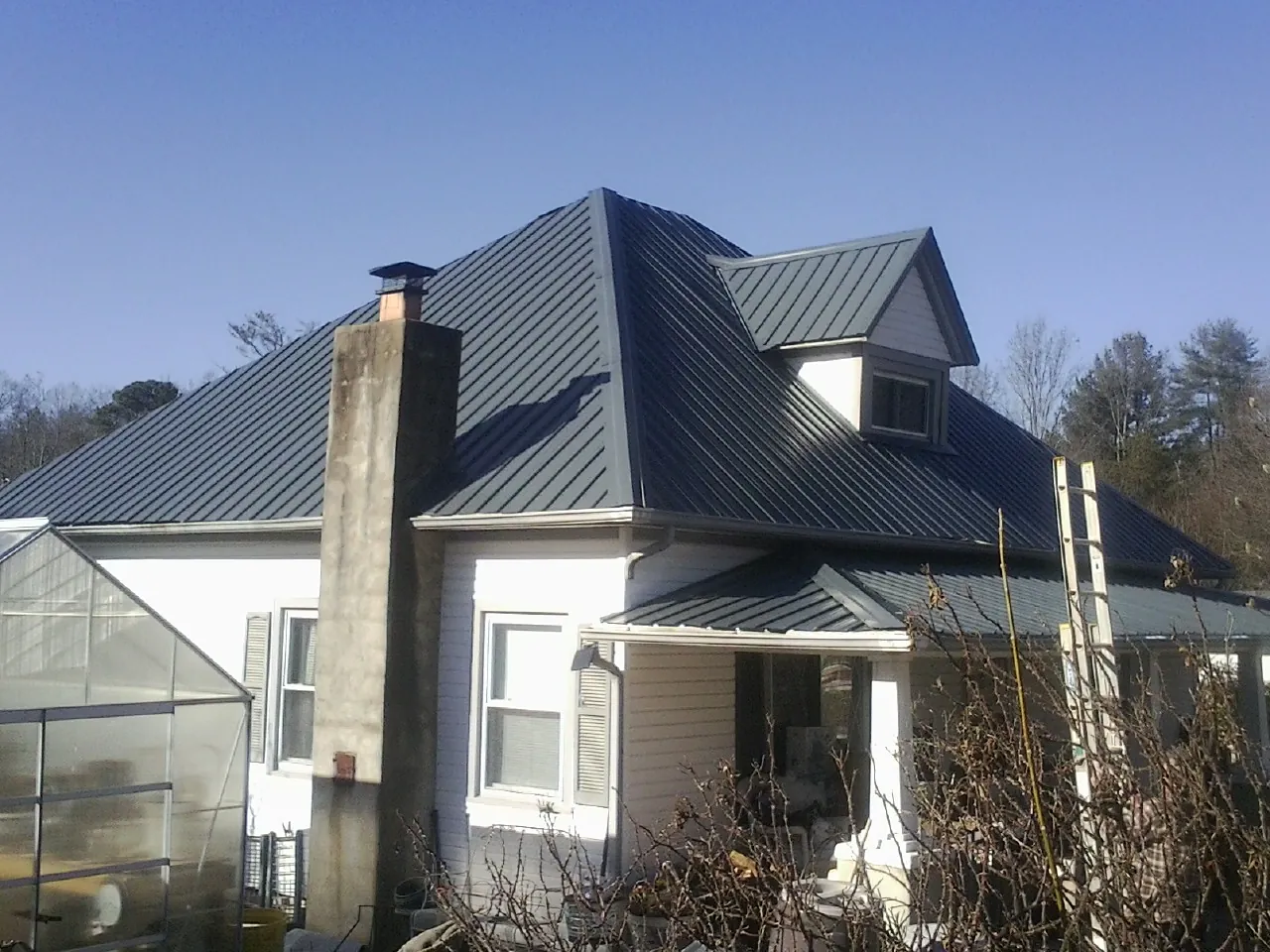 Dark blue standing seam metal roof on a white farmhouse with dormer — Slate & Tile Roof Repair by Roofing Brothers in Fingerville