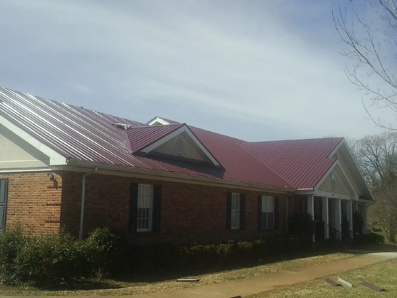 Red metal roof with gabled entries on a long brick building, from a Hail Damage Roof Repair job in Fingerville