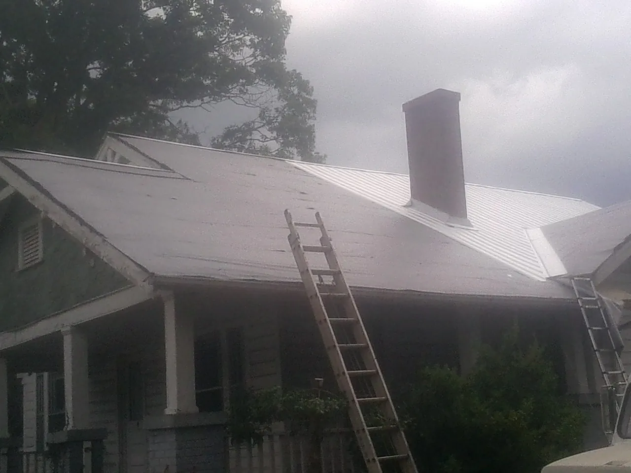 Ladders against a metal roof on an older home with a brick chimney in Fingerville