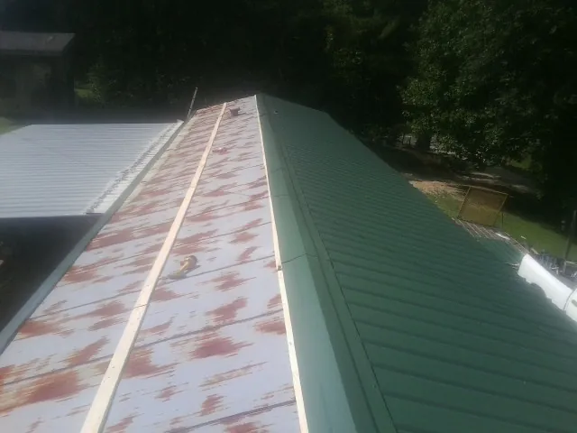 Old rusted panels beside newly installed green metal roofing — Wind Damage Roof Repair by Roofing Brothers in Fingerville