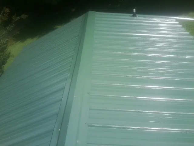 New green metal panels meeting at the ridge of a roof — Flat Roof Repair work by our crew in Fingerville
