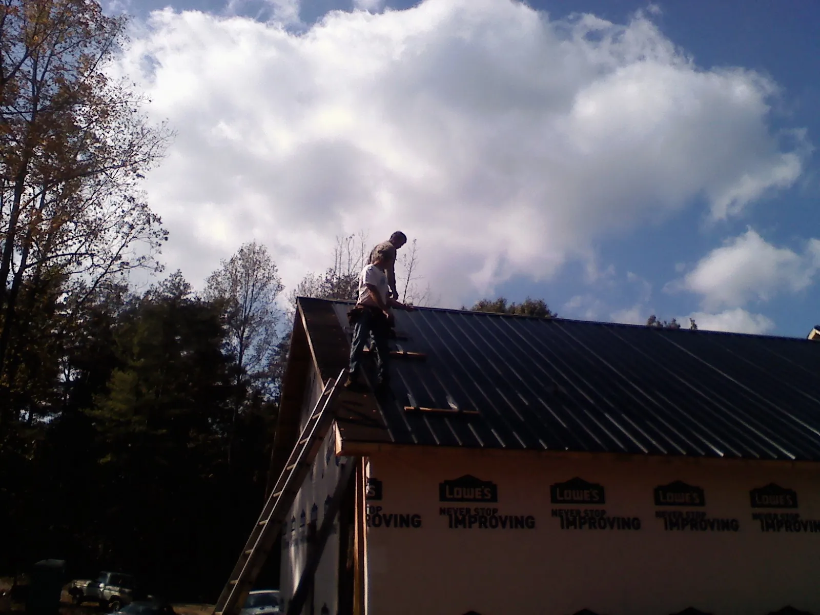Roofer fastening dark metal panels high against a cloudy sky, from a Roof Inspection job in Fingerville