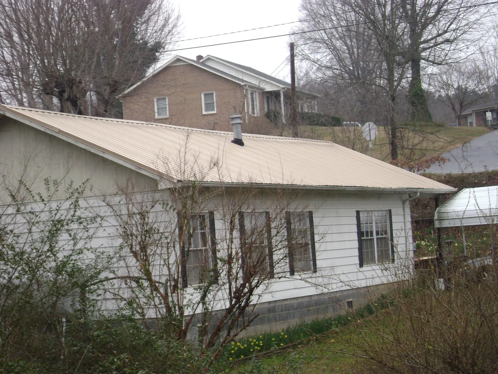Tan metal roof on a white sided house set into a hillside — Commercial Roofing by Roofing Brothers in Fingerville