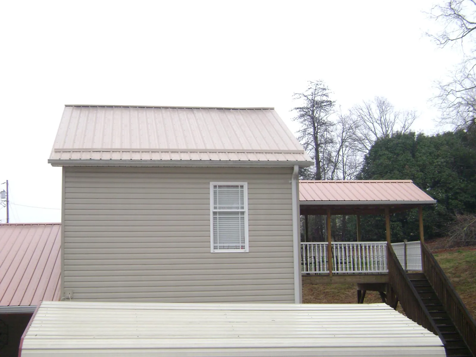 Tan metal roofs on a two story addition and attached porch, from a Roof Replacement job in Fingerville